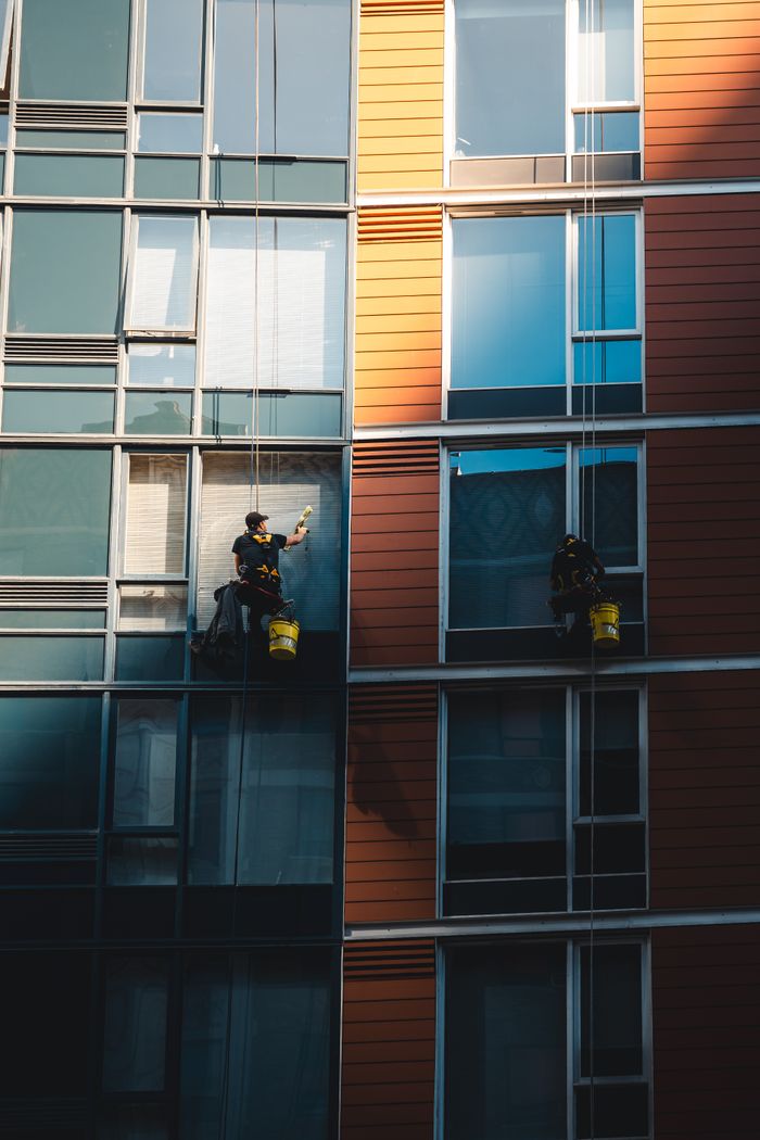 Deux travailleurs suspendus pour nettoyer les vitres d’une façade de gratte-ciel moderne.